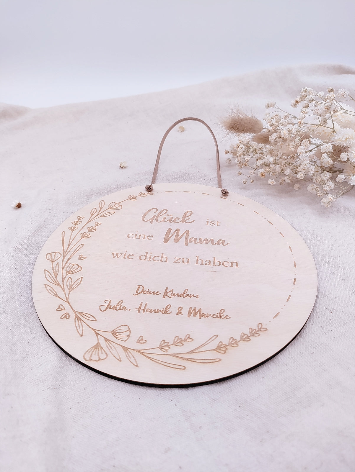 Personalisiertes Muttertags-Schild aus Birkensperrholz mit Gravur „Glück ist eine Mama wie dich zu haben“, verziert mit Blumenranke und veganer Lederschnur zum Aufhängen. Ein einzigartiges Geschenk zum Muttertag.